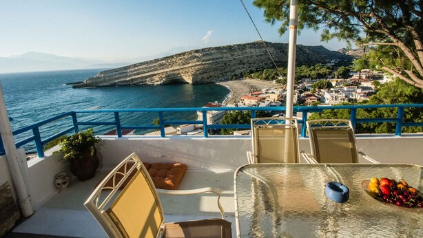 Un balcón con vistas despejadas al mar, una silla, una mesa con fruta y una planta en maceta.