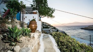 Una propiedad costera con un estrecho sendero de piedra que conduce a un edificio blanco con detalles azules, con vistas al mar.