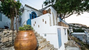 Un edificio blanco con contraventanas azules y una gran maceta de terracota al frente.