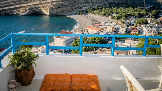 A balcony with a view of a coastal town, a potted plant, and a polka-dotted cushion. - Castri House in Matala (Matala)