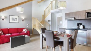 Ein modernes Wohnzimmer mit einem roten Sofa, einem Esstisch mit Stühlen und einer Küchenzeile inklusive Mikrowelle und Herd.