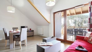 Eine moderne Wohnung mit Essbereich, einem Wohnzimmer mit rotem Sofa und einem Balkon mit Blick auf Bäume.
