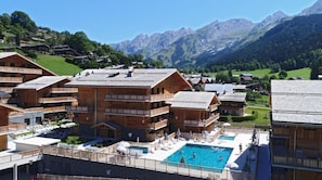 A resort with wooden buildings, a swimming pool, and a mountainous backdrop. - Wifi, swimming pool, sauna, hammam, tv, ski locker, 42-47m², La Clusaz (La Clusaz)