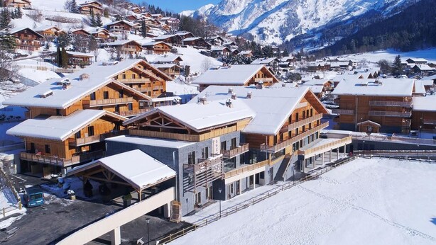 A snow-covered mountain resort with wooden buildings, ski slopes, and a clear view of the mountains.