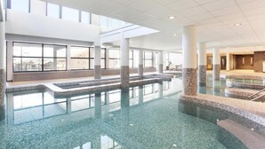 A large indoor swimming pool with clear water, tiled steps, and a high ceiling with natural light.