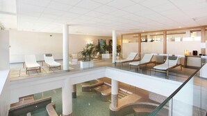 A spacious lobby with multiple lounge areas, a central water feature, and a glass railing overlooking a lower level.