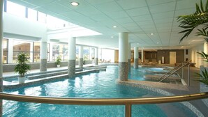 An indoor swimming pool with clear water, surrounded by columns and potted plants.