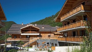 A wooden chalet with multiple balconies, a central staircase, and a mountain backdrop.