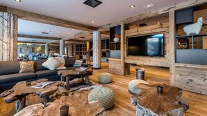A spacious living area with a large TV, wooden furniture, and a stone wall in the background.