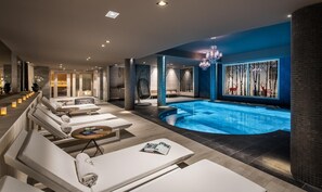 Uma área interna de piscina moderna, com espreguiçadeiras e um espaço para sentar.