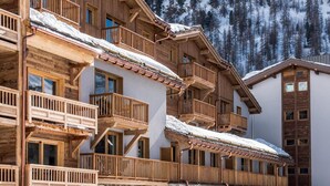 A multi-story wooden building with balconies, stone arches, and a snowy mountain backdrop.