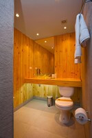Un baño con paredes y encimera de madera, un inodoro, un cubo de basura y un perchero para toallas.