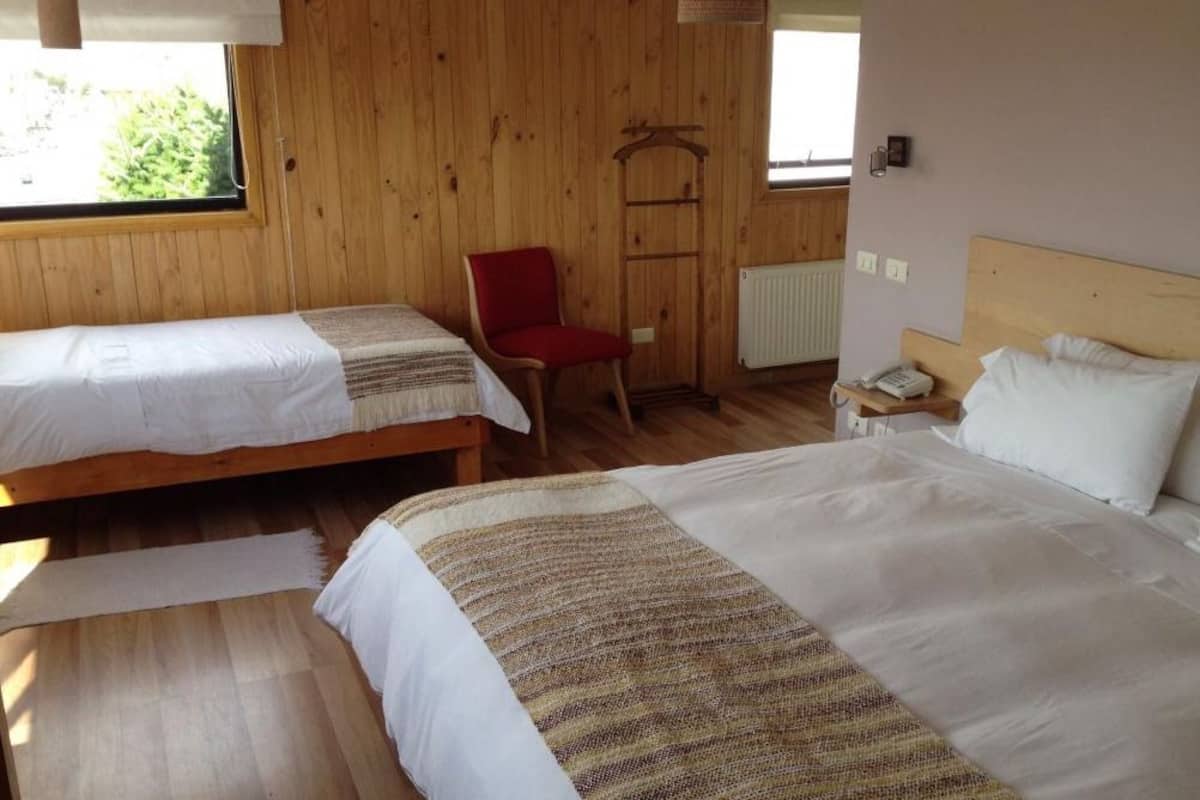 A room with two single beds, a red chair, a wooden ladder, and a window with a view of greenery.