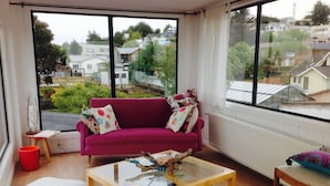 A living room with a large window, a red sofa, a glass coffee table, and a laptop on the floor. - Hotel Ilaia (Punta Arenas)