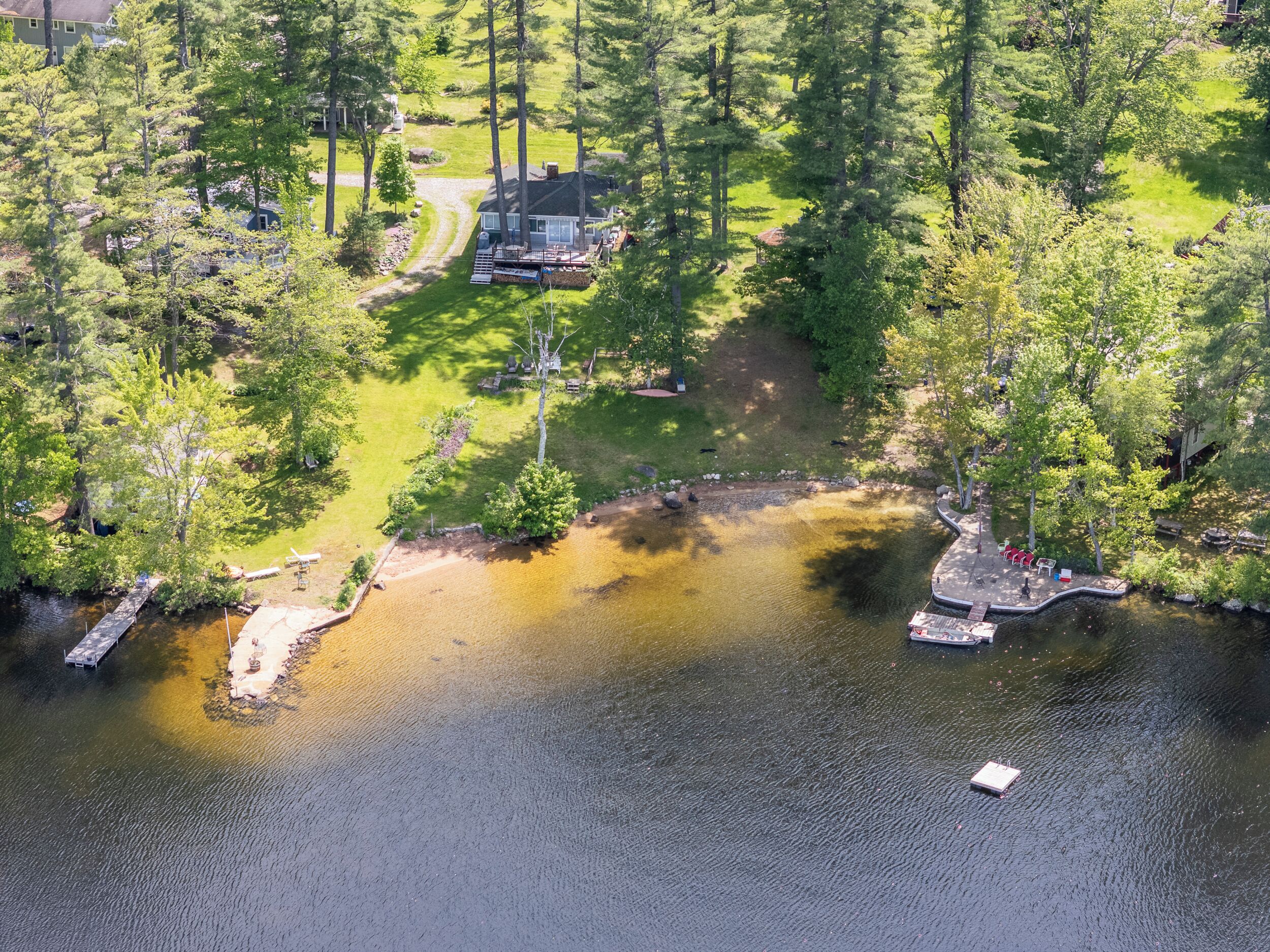 Ett flygbildsfoto av en fastighet vid en sjö, med ett hus, en brygga och omgivande grönska.