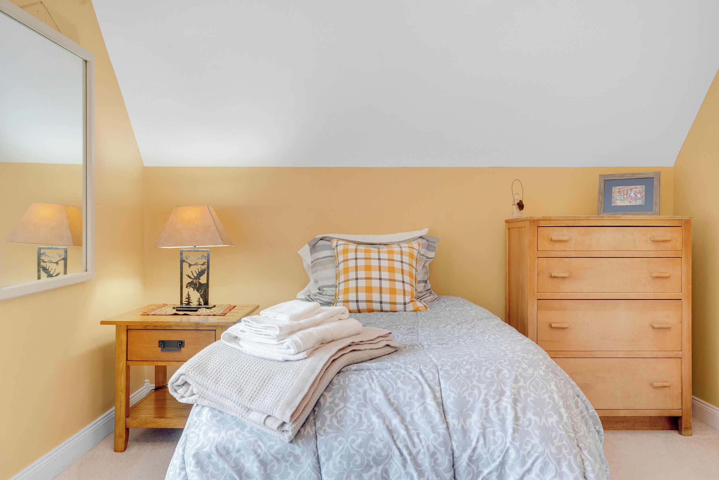 Een slaapkamer met een bed, een nachtkastje met een lamp, een kast en een spiegel.