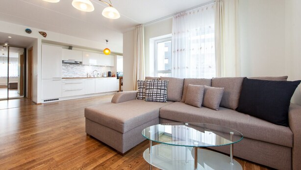 Una sala de estar moderna con un sofá seccional, una mesa de centro de vidrio y una cocina al fondo.