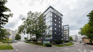 Un edificio moderno de varios pisos con fachada de vidrio, rodeado de árboles y un cielo despejado.