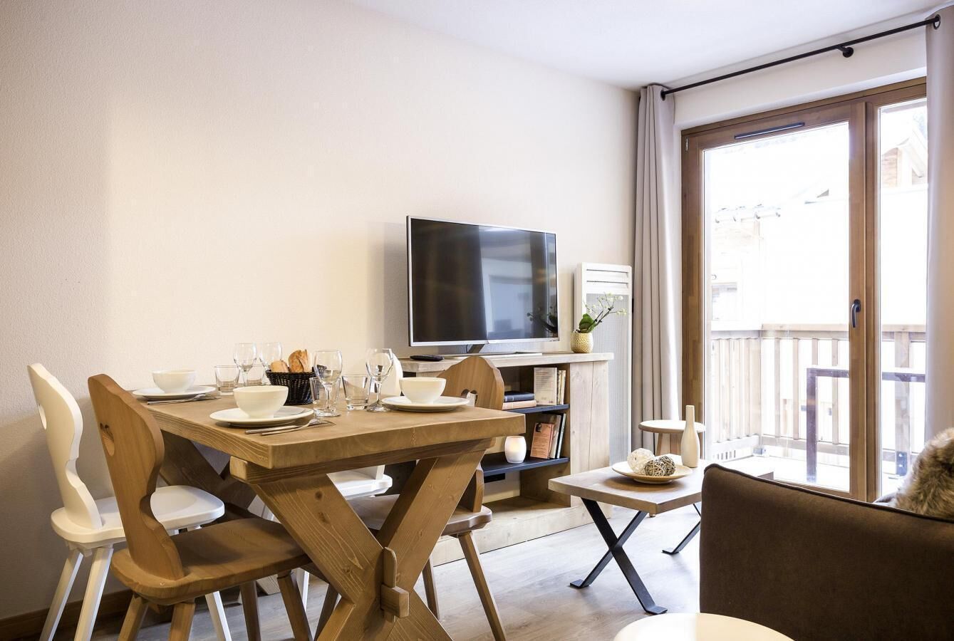 A dining area with a wooden table set for four, a television, and a balcony with a view.