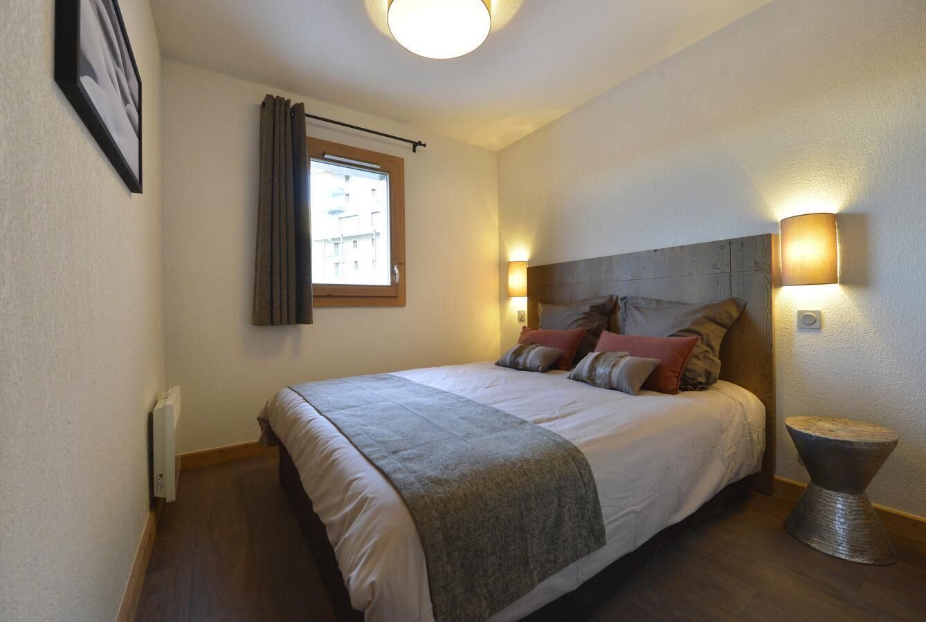 A bedroom with a bed, a bedside lamp, a window with curtains, and a radiator.