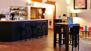 A bar area with a counter, stools, and a table with chairs. There is a fire extinguisher on the wall and a framed picture above the table.