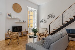 Una sala de estar moderna con un sofá, televisión, sillas de mimbre, una mesa de centro y una escalera con barandilla.