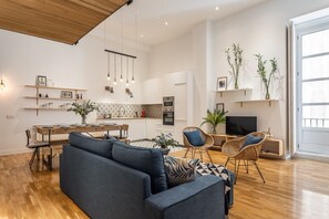 A modern living room with a sofa, chairs, a dining table, and a kitchen area with cabinets and a TV.