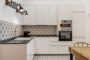 Una cocina moderna con armarios blancos, encimera negra, cafetera, horno y una mesa de comedor de madera.