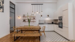 Una cocina moderna con armarios blancos, una mesa de comedor de madera e iluminación colgante.
