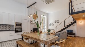 Una cocina moderna con armarios blancos, una mesa de comedor de madera y una escalera que sube a un nivel superior.