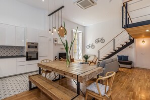 Una cocina moderna con armarios blancos, una mesa de comedor de madera y una escalera que sube a un nivel superior.