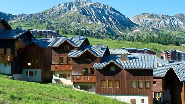 Une rangée de bâtiments de style chalet en bois, avec des toits inclinés, se dressant sur un fond de montagnes.