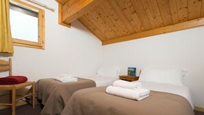 Une chambre avec deux lits, un plafond en bois, une fenêtre, une chaise et une petite table sur laquelle se trouve un livre.