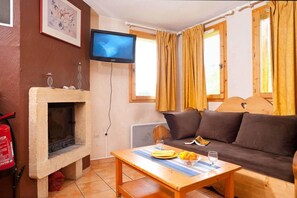 Ein gemütliches Wohnzimmer mit Kamin, einer Couch, einem Fernseher und einem Tisch mit Früchten und einem Glas.