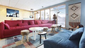 Un salon moderne avec un canapé rouge, un canapé bleu et une table basse blanche. Une grande fenêtre offre une vue sur les montagnes.