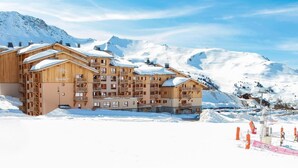 Un immeuble en bois à plusieurs étages, doté de balcons, se dressant sur fond de montagnes enneigées.