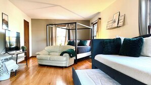 A modern, well-lit room with a large bed, a sofa, a TV, and a four-poster bed. - Hot Tub | Sauna | 1.1 MI to ND  | Backyard Oasis (South Bend)