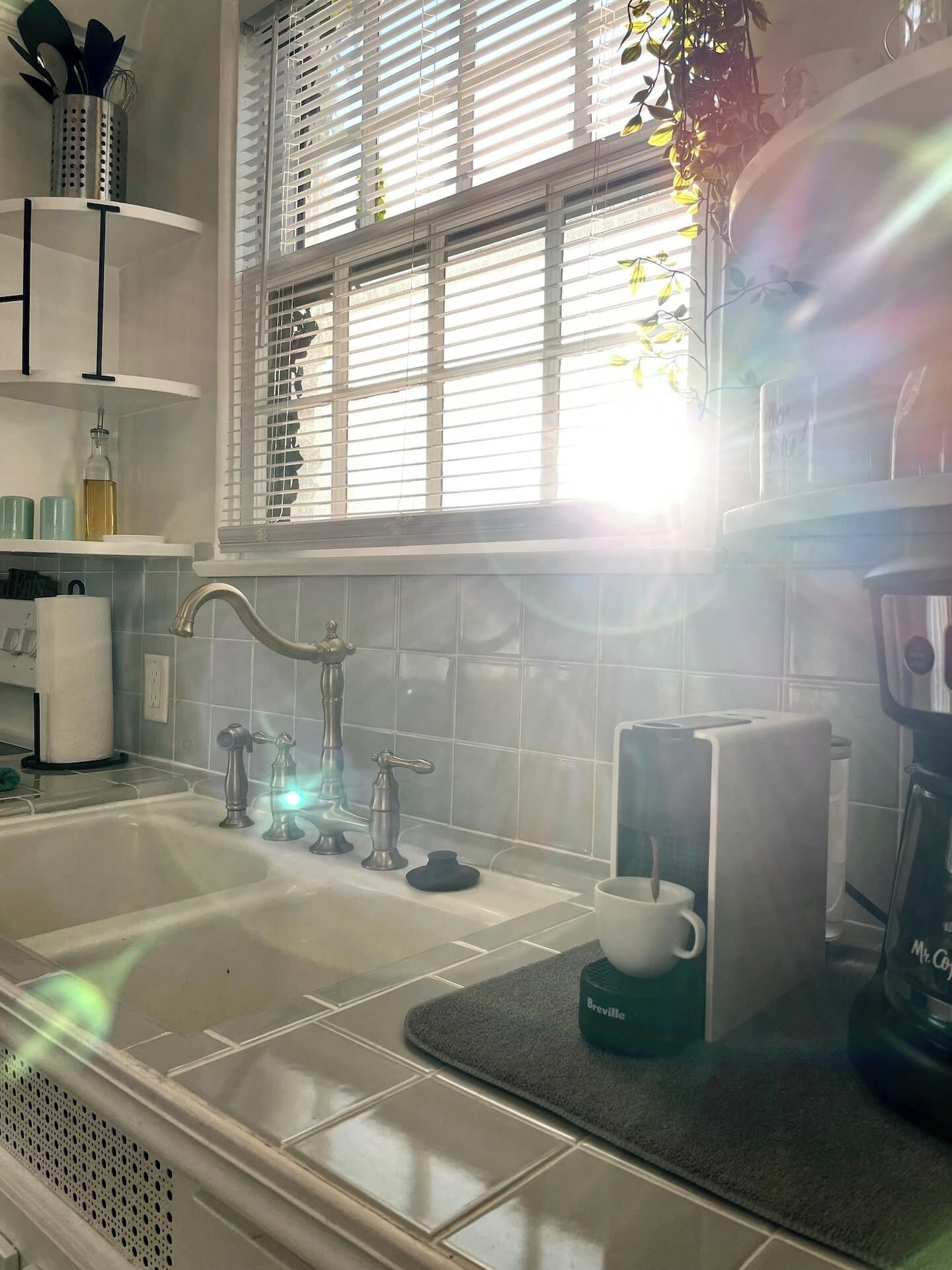 A kitchen with a sink, two faucets, a coffee maker, and a window with blinds.