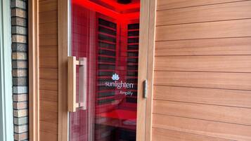 A wooden sauna with a glass door, a logo, and a red interior.