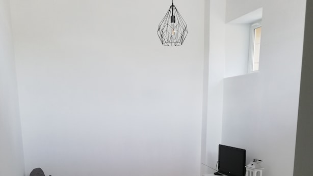 A modern living room with a sectional sofa, a small white table, a TV on a white stand, and a hanging light fixture. - Charming Duplex 4 people (FLEURY-SUR-ORNE)