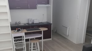 A compact kitchen with modern appliances, a small dining area, and a white table with a patterned table runner. - Charming Duplex 4 people (FLEURY-SUR-ORNE)