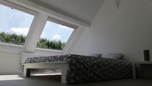 A bedroom with a skylight, a bed with patterned bedding, and a bedside table. - Charming Duplex 4 people (FLEURY-SUR-ORNE)
