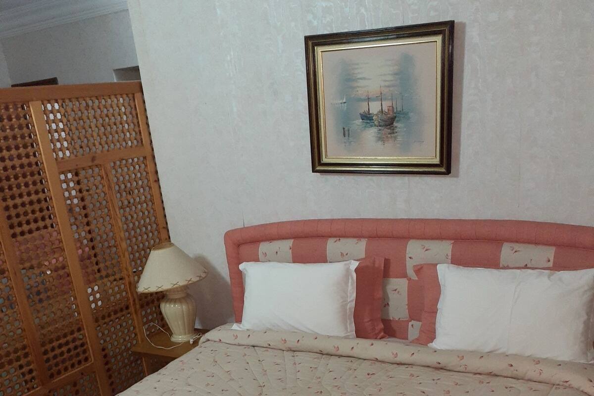 Ein ordentlich bezogenes Bett mit einem blumigen Überwurf, einem hölzernen Kopfseitenverkleidung und einem gerahmten Bild an der Wand.