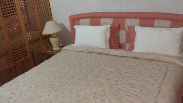 A neatly made bed with a floral-patterned bedspread, a wooden headboard, and a framed picture on the wall.