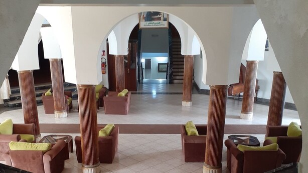 Um hall amplo com uma escadaria central, ladeado por áreas de estar e colunas.