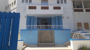 Um hotel chamado "HOTEL DE L'ATLANTIDE" com fachada azul, entrada decorativa e escadaria que leva à entrada.