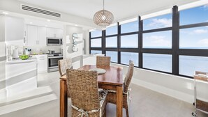 Una cocina moderna con armarios blancos, microondas y un comedor con sillas de mimbre y una mesa de madera.
