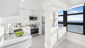 Una cocina moderna con armarios blancos, electrodomésticos de acero inoxidable y un amplio ventanal con vista al mar.