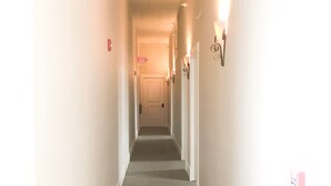 A narrow, well-lit hallway with a carpeted floor, white walls, and a door at the end. - Inn On Central (Le Mars)
