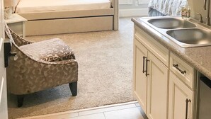 A bedroom with a bed, a bedside table, a chair, a large mirror, and a window. - Inn On Central (Le Mars)